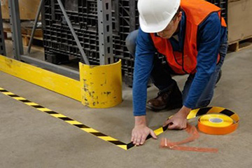 Un trabajador marcando un área en una planta de manufactura con cinta de rayas negras y amarillas.